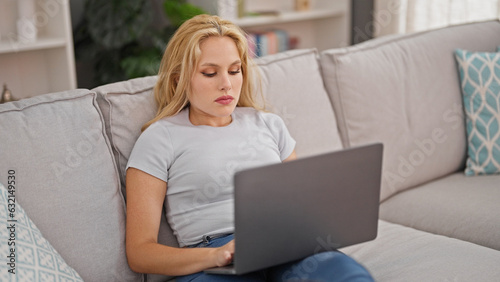 Young blonde woman using laptop sitting on sofa at home