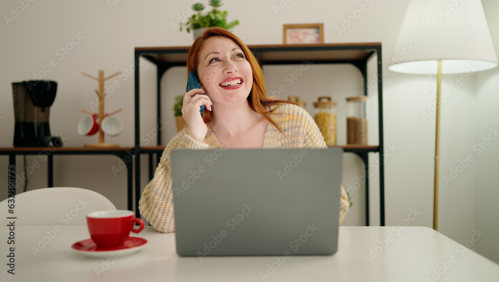 Young redhead woman using laptop and talking on the smartphone at home Young redhead woman using laptop and talking on the smartphone at home