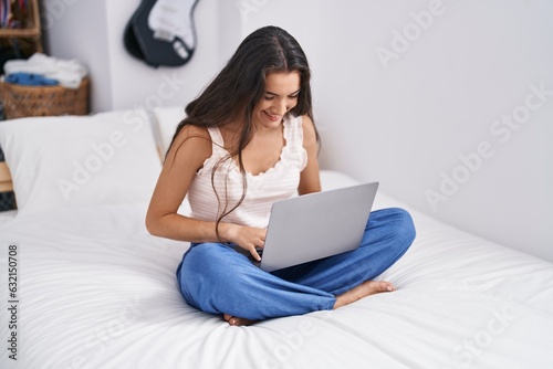 Young hispanic woman using laptop sitting on bed at bedroom