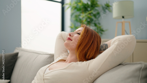 Young redhead woman relaxed with hands on head sitting on sofa at home