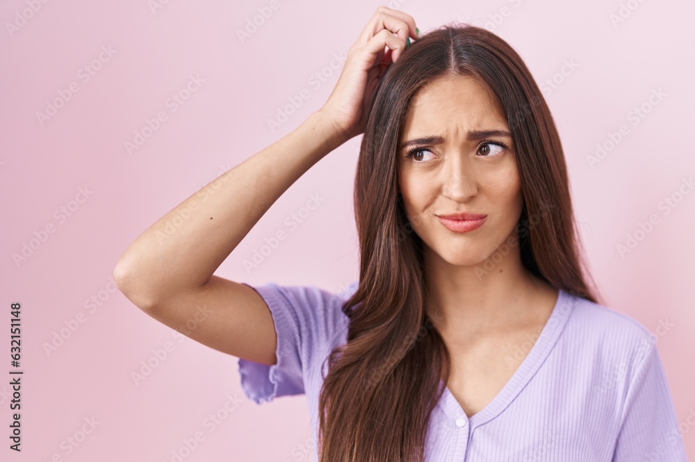 Young hispanic woman with long hair standing over pink background confuse and wondering about question. uncertain with doubt, thinking with hand on head. pensive concept. Young hispanic woman with long hair standing over pink background confuse and wondering about question. uncertain with doubt, thinking with hand on head. pensive concept.