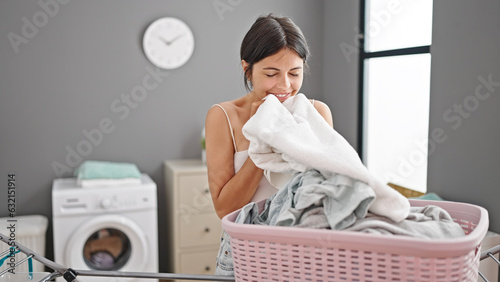 Young beautiful hispanic woman smiling confident smelling clean clothes at laundry room