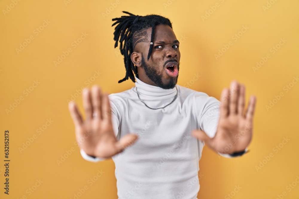 African man with dreadlocks wearing turtleneck sweater over yellow background doing stop gesture with hands palms, angry and frustration expression African man with dreadlocks wearing turtleneck sweater over yellow background doing stop gesture with hands palms, angry and frustration expression