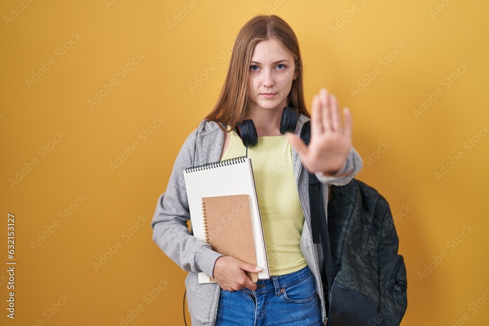 Young caucasian woman wearing student backpack and holding books doing stop sing with palm of the hand. warning expression with negative and serious gesture on the face. Young caucasian woman wearing student backpack and holding books doing stop sing with palm of the hand. warning expression with negative and serious gesture on the face.