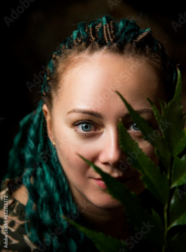 portrait of a beautiful woman with green hair and blue eyes with green leaves in dark studio