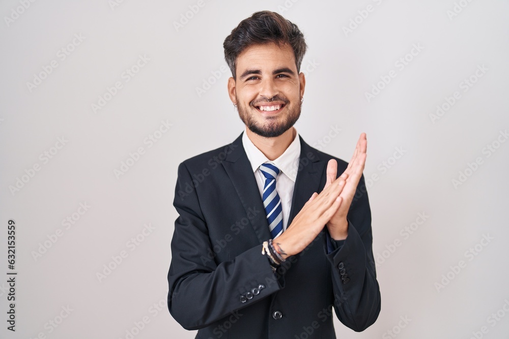 Young hispanic man with tattoos wearing business suit and tie clapping and applauding happy and joyful, smiling proud hands together Young hispanic man with tattoos wearing business suit and tie clapping and applauding happy and joyful, smiling proud hands together