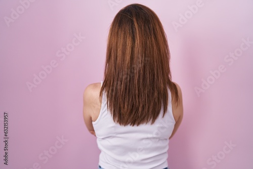 Brunette woman standing over pink background standing backwards looking away with crossed arms