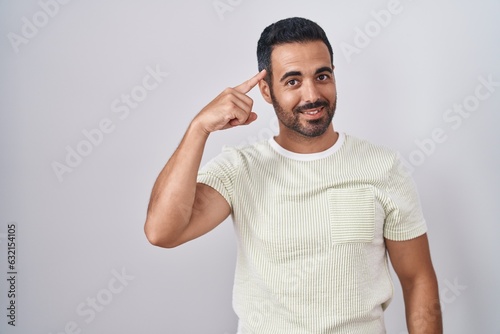 Hispanic man with beard standing over isolated background smiling pointing to head with one finger, great idea or thought, good memory