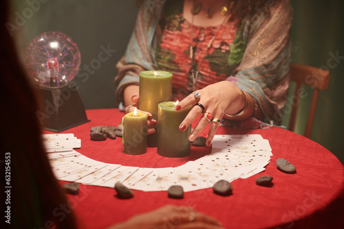 Hands of fortune teller putting burning wax candles on table and spreding tarot cards photo