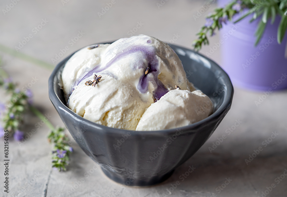 Lavender ice cream in a grey bowl with lavender syrup on the top, lavender branches in purple vase over grey concrete background
