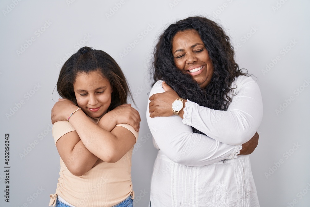 Mother and young daughter standing over white background hugging oneself happy and positive, smiling confident. self love and self care Mother and young daughter standing over white background hugging oneself happy and positive, smiling confident. self love and self care
