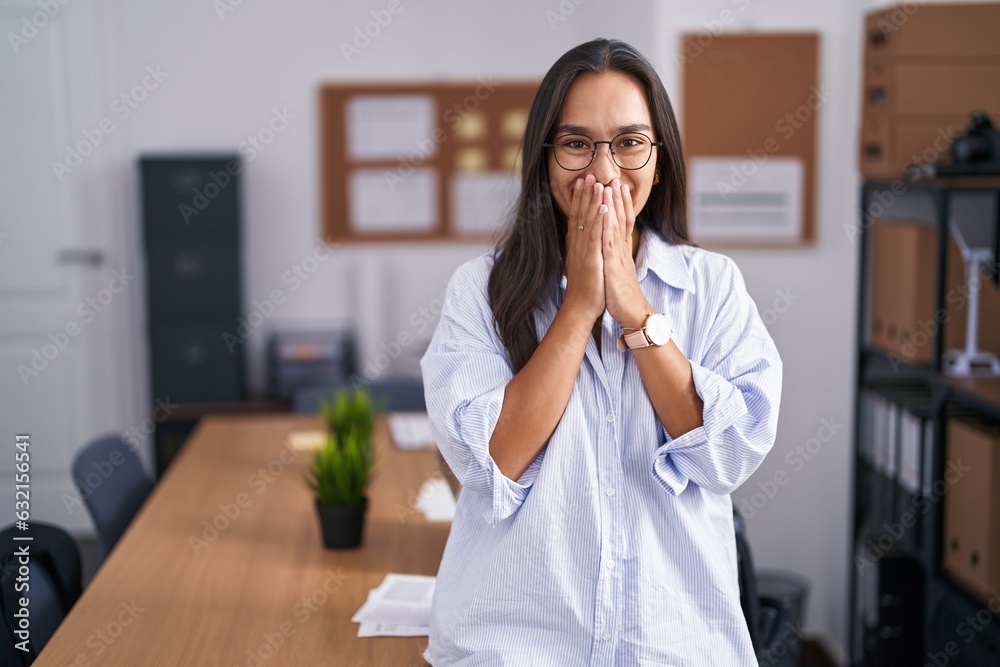 Young hispanic woman at the office laughing and embarrassed giggle covering mouth with hands, gossip and scandal concept Young hispanic woman at the office laughing and embarrassed giggle covering mouth with hands, gossip and scandal concept