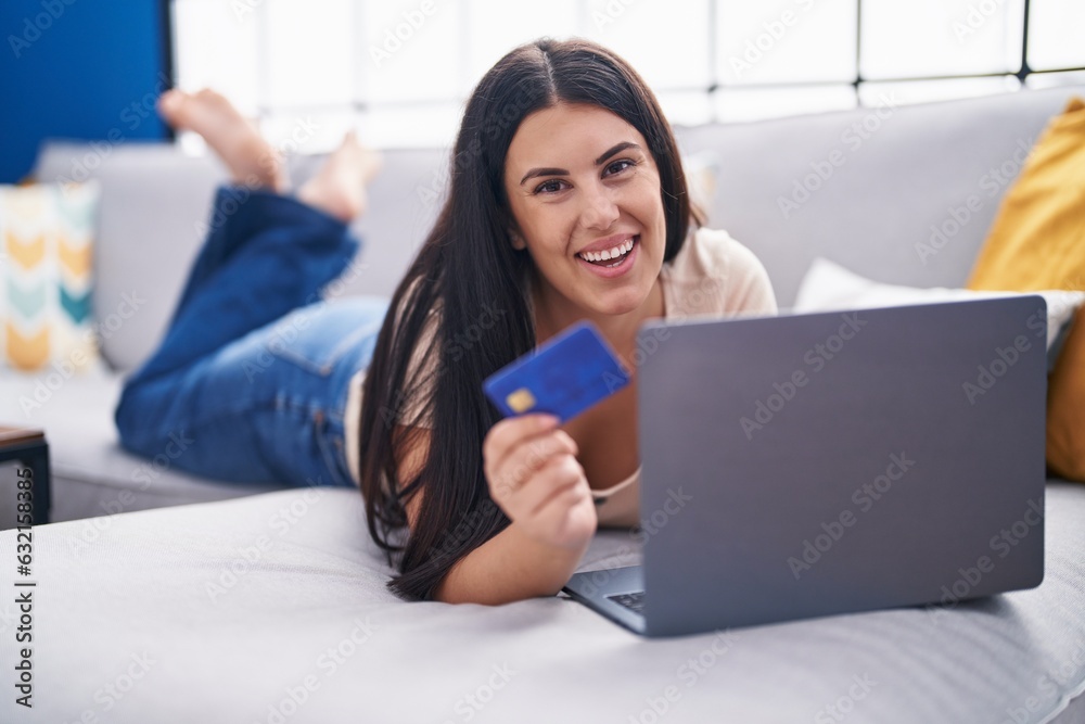 Young beautiful hispanic woman using laptop and credit card lying on sofa at home Young beautiful hispanic woman using laptop and credit card lying on sofa at home