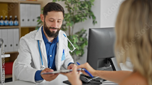 Young hispanic man doctor giving contract to patient to sign at the clinic