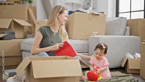 Mother and daughter writing on notebook checking playing on floor at new home