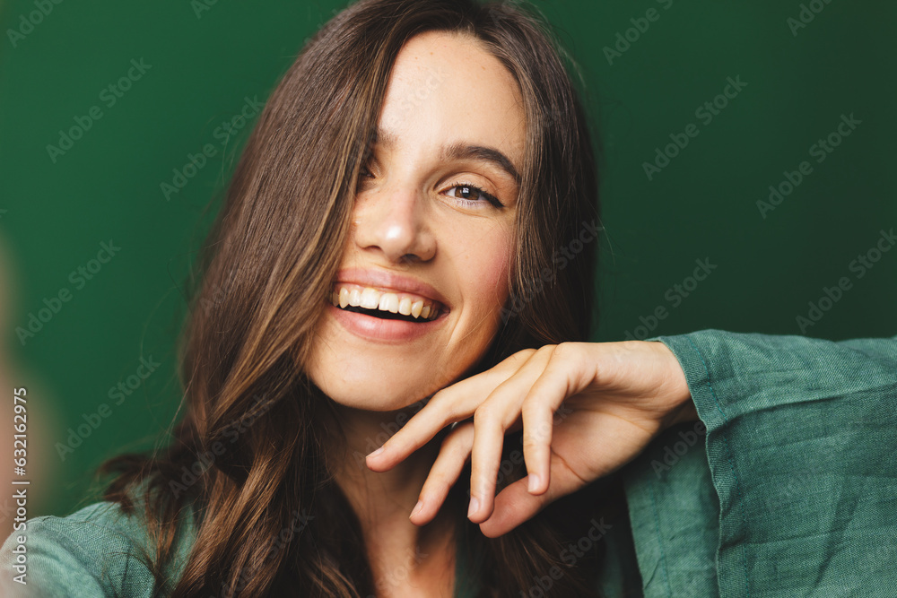 Portrait of young happy brunette curly hair woman with toothy smile laughing isolated over green wall background make selfie looking camera. Portrait of young happy brunette curly hair woman with toothy smile laughing isolated over green wall background make selfie looking camera.