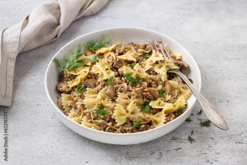 Traditional Jewish dish kasha varnishkes: buckwheat, pasta, champignon mushrooms, fried onions with herbs on a gray textured background, vegan food photo