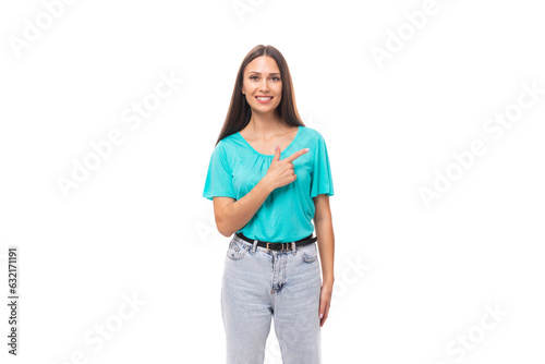 young well-groomed caucasian brunette woman with long hair in a blue t-shirt points her hand to the side on an isolated white background with copy space