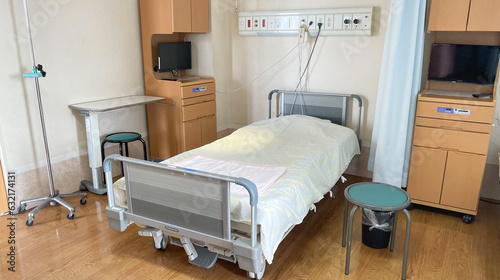 A multi-bed hospital room with an empty bed ready for a new patient with a cabinet, TV, and hospital equipment in a Japanese hospital. 
