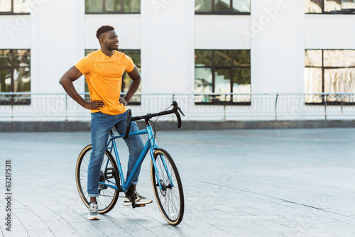 Dark skinned handsome man walking street near bicycle while looking away