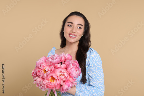 Beautiful young woman with bouquet of pink peonies on beige background