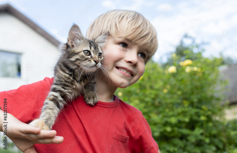 striped fluffy kitten sits on the shoulder of a cute boy of 7 years old, looking in one