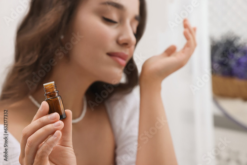 Beautiful young woman with bottle of essential oil indoors, selective focus