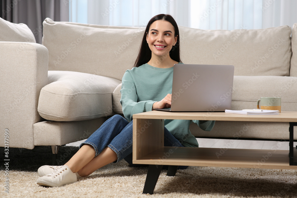 Happy woman working with laptop at coffee table in living room Happy woman working with laptop at coffee table in living room