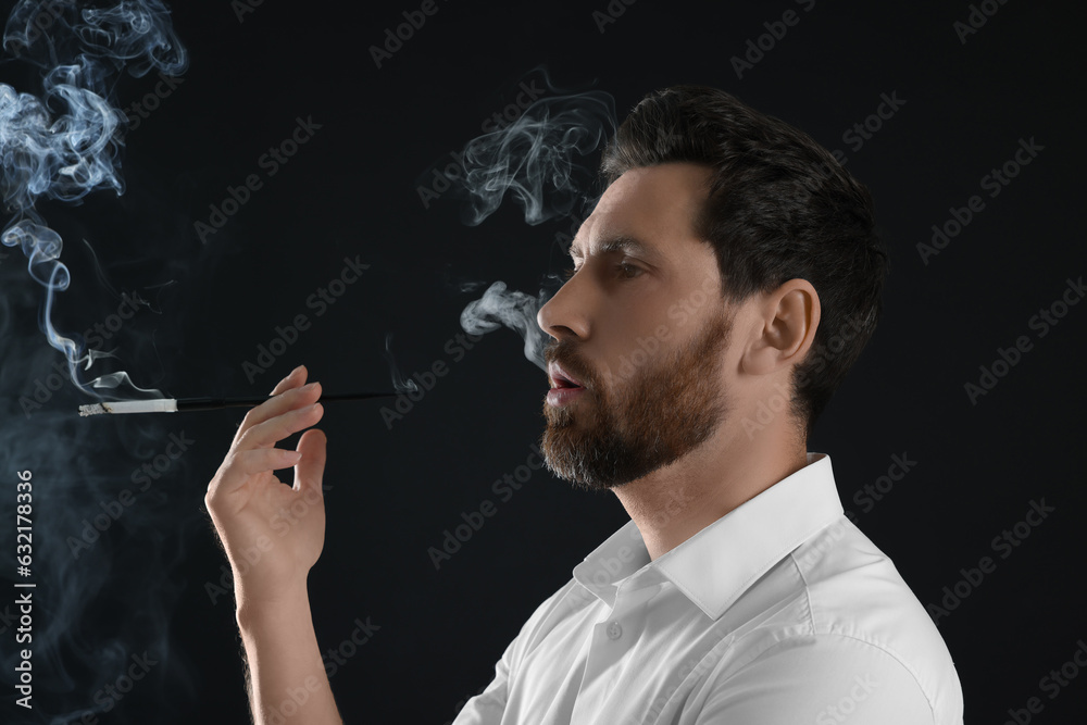 Fototapeta premium Man using long cigarette holder for smoking on black background