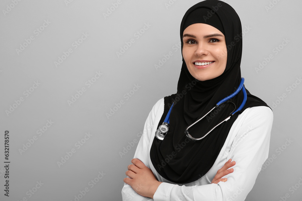 Muslim woman wearing hijab and medical uniform with stethoscope on light gray background, space for text