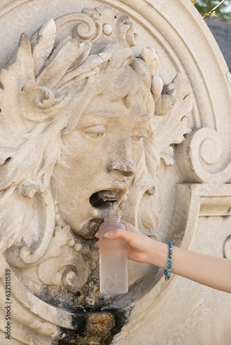 Canvas Print A girl pouring water in a bottle from a drinking fountain in the form of a human face in Austria