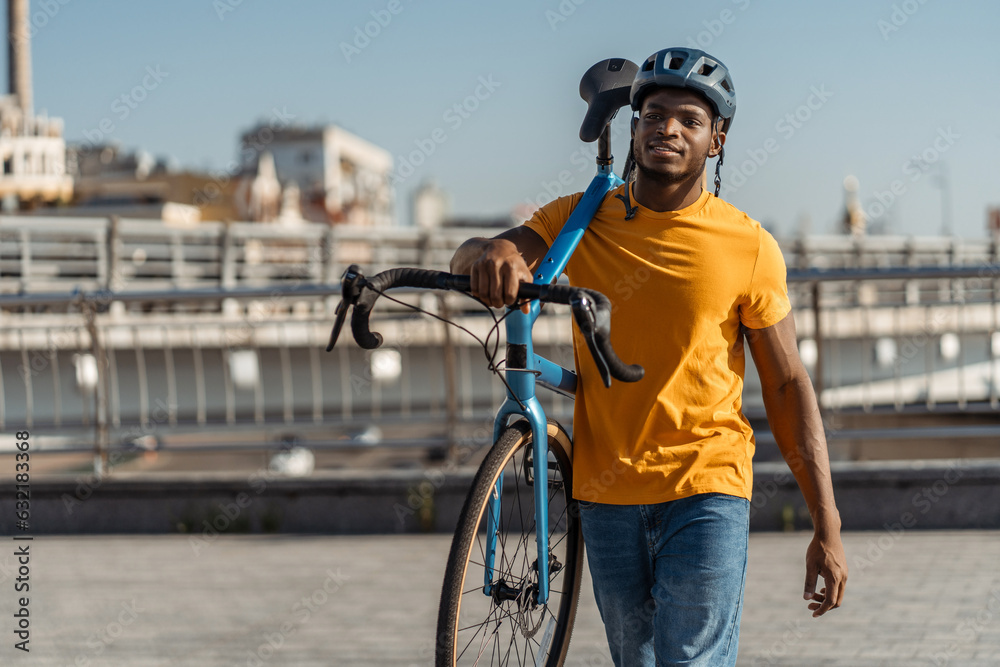 Portrait of handsome smiling African American man wearing helmet holding his bicycle