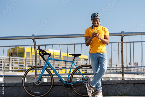 Fototapeta Naklejka Na Ścianę i Meble -  Smiling African American man in helmet holding mobile phone looking at screen