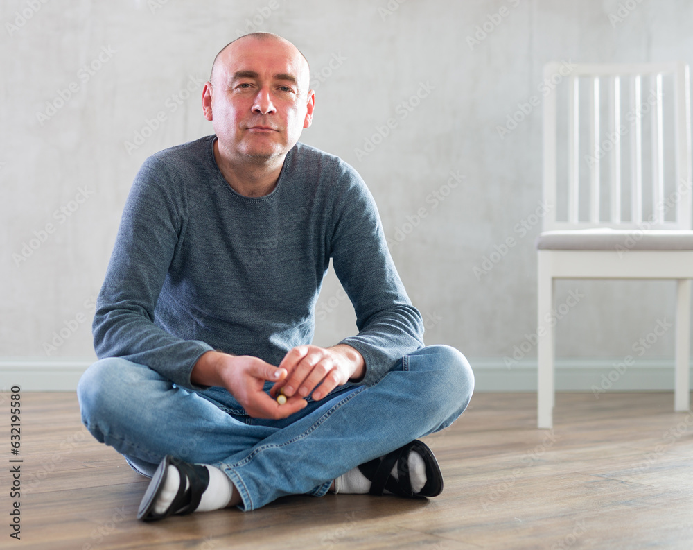 Portrait of confident middle-aged man in casual clothes sitting on the floor in living room Portrait of confident middle-aged man in casual clothes sitting on the floor in living room