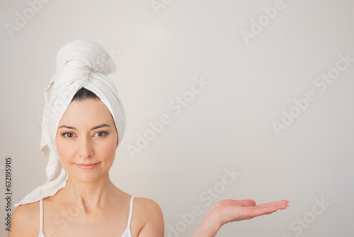photo of a young pretty woman in white underwear with a white towel smiling, holding something in her hand and looking at the camera.Space for copying.Demonstration and advertising of beauty products