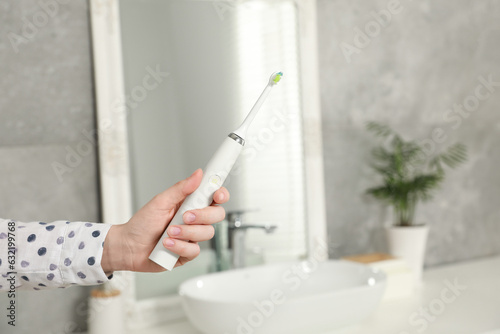 Woman holding electric toothbrush in bathroom at home  closeup