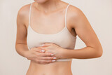 young woman in beige underwear holds her stomach with her hands, feels pain, isolated on a beige background