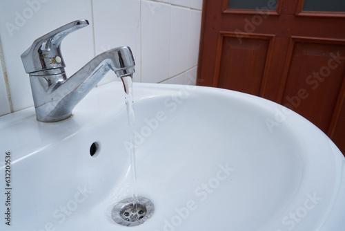 metallic faucet with running water in a white bathroom