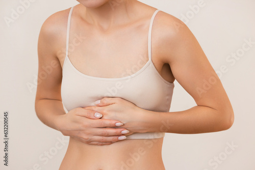 young woman in beige underwear holds her stomach with her hands, feels pain, isolated on a beige background © Ольга Шефер