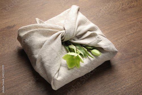 Furoshiki technique. Gift packed in white fabric decorated with beautiful flowers on wooden table