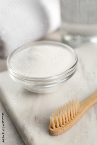Bamboo toothbrush and glass bowl of baking soda on marble board, closeup