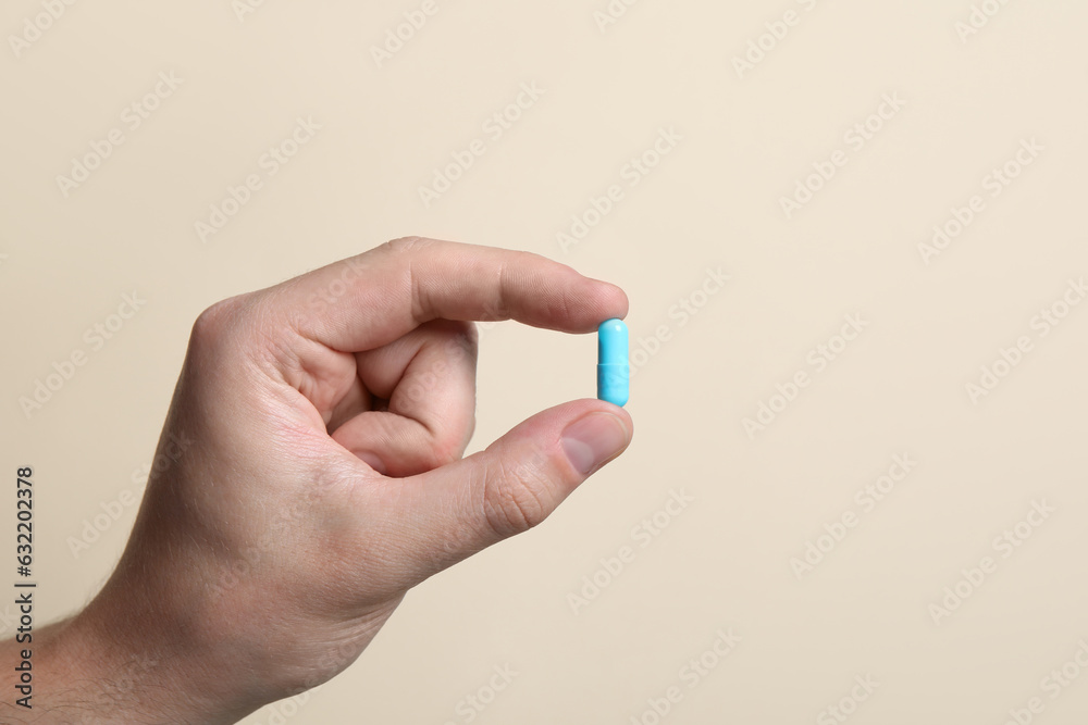 Man holding pill on beige background, closeup Man holding pill on beige background, closeup