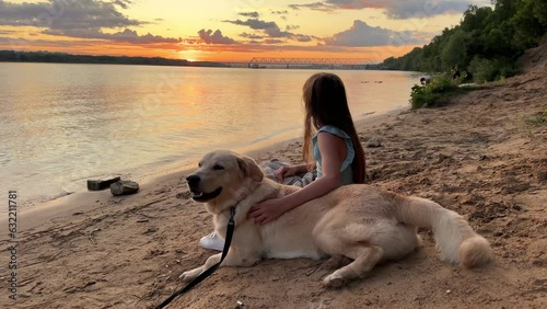 Best friends - a child and a dog sit together, a child leans against the dog, and both enjoy the sunset on the river bank photo