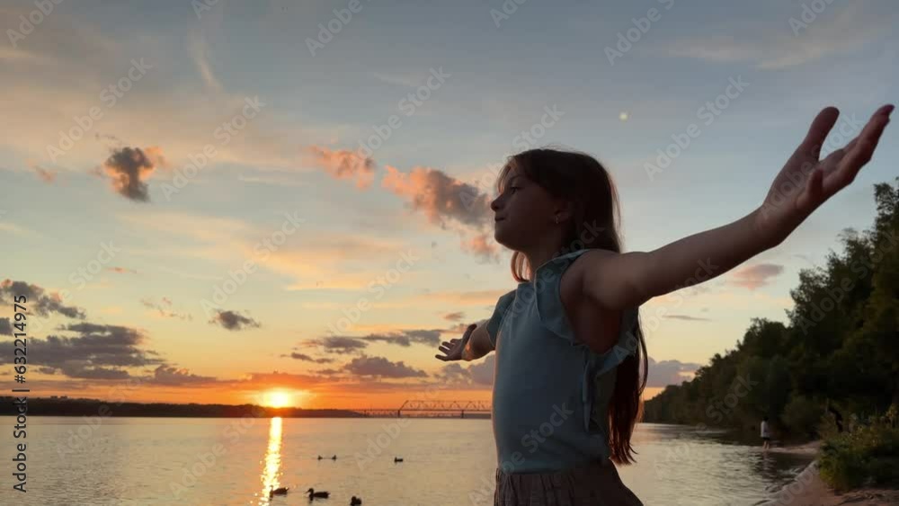 a happy relaxed girl breathes fresh air at sunset, raising her hands above the blue sky in summer, dreaming of freedom, a child raises her hands up in nature
