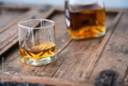 Glass of wiski or scotch on wooden barrel with blurred bottle in background photo