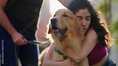 Woman embracing her Golden Retriever Dog outside at park. Couple enjoying weekend activity. Person hugs pet outdoors in sunlight