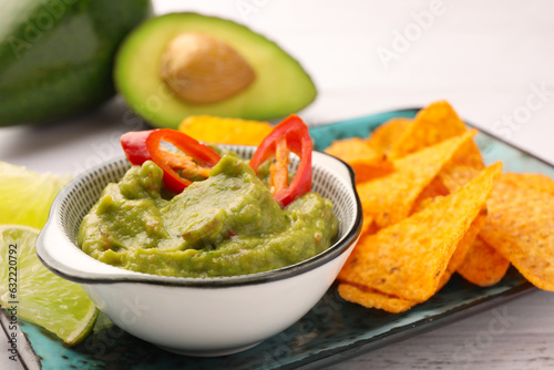 Bowl of delicious guacamole with chili pepper and nachos chips on white wooden table, closeup