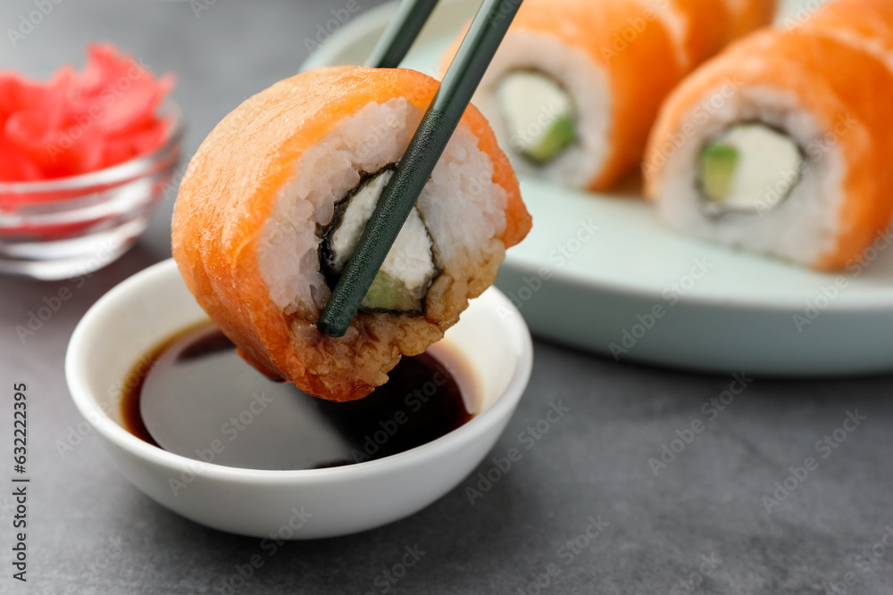 Dipping tasty sushi into soy sauce at grey table, closeup Dipping tasty sushi into soy sauce at grey table, closeup