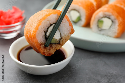 Dipping tasty sushi into soy sauce at grey table, closeup