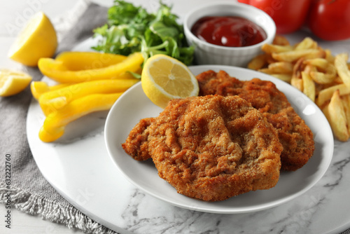 Tasty schnitzels served with potato fries, ketchup and vegetables on marble board, closeup
